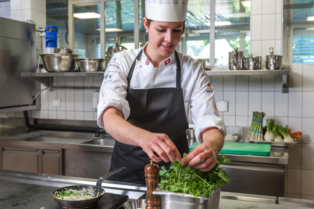 Une cuisinière agrémente un plat de fines herbes.