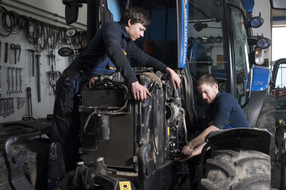 Deux jeunes techniciens réparent le moteur d'un tracteur.