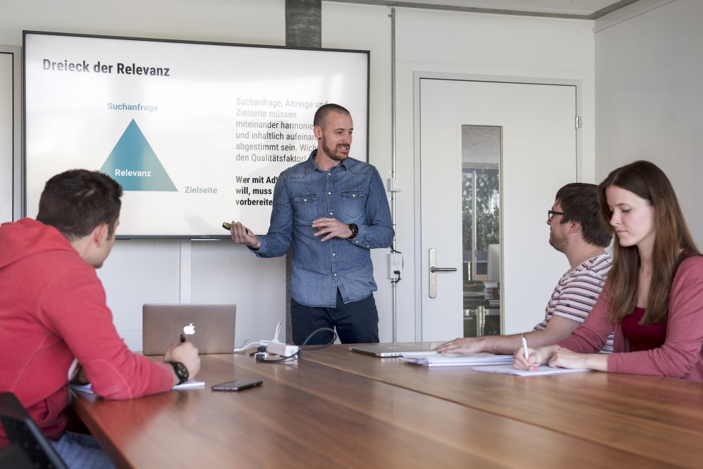 Un homme devant un écran montre un schéma à ses collaborateurs lors d’une séance de travail.