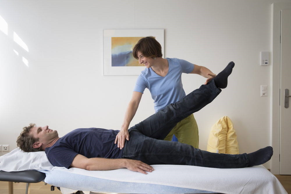Une physiothérapeute mobilise la jambe d’un patient lors d’un exercice.
