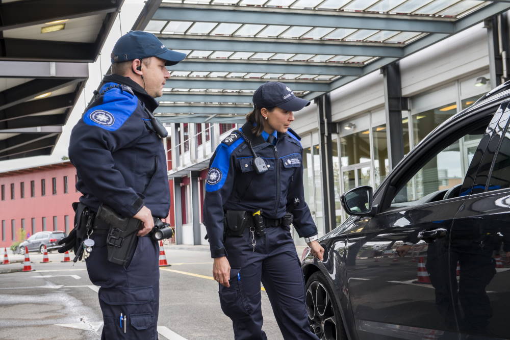 Un homme et une femme travaillant pour la douane et la sécurité des frontières arrêtent un véhicule à un poste-frontière.