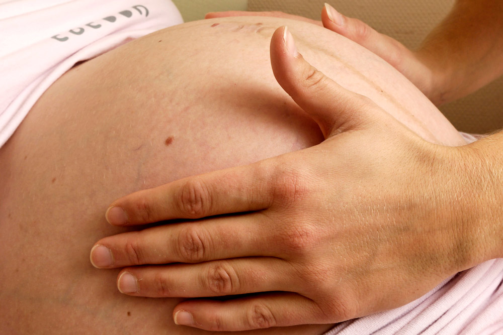 Des mains palpent le ventre d'une femme enceinte