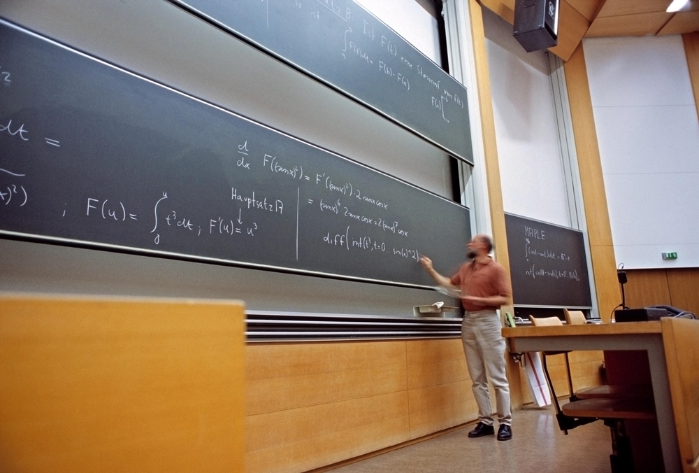 Homme écrivant des formules mathématiques sur un tableau noir