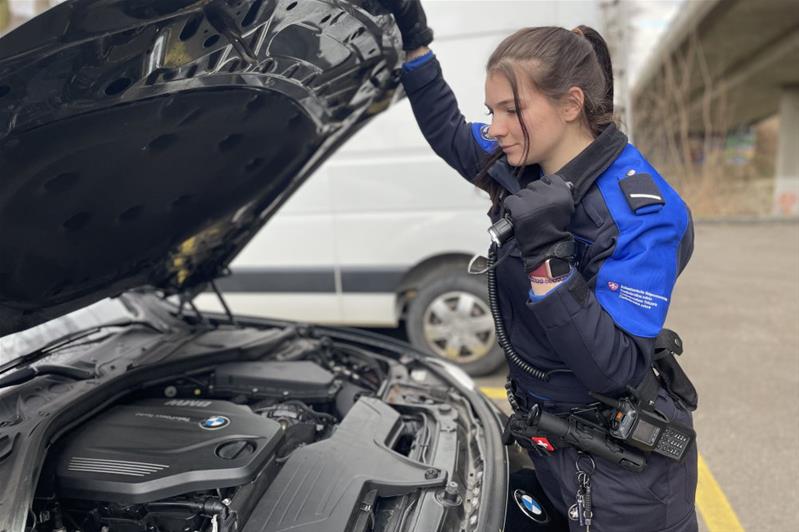 Une jeune femme en uniforme de l'Office fédéral de la douane et sécurité des frontières arrête un véhicule à un poste-frontière.