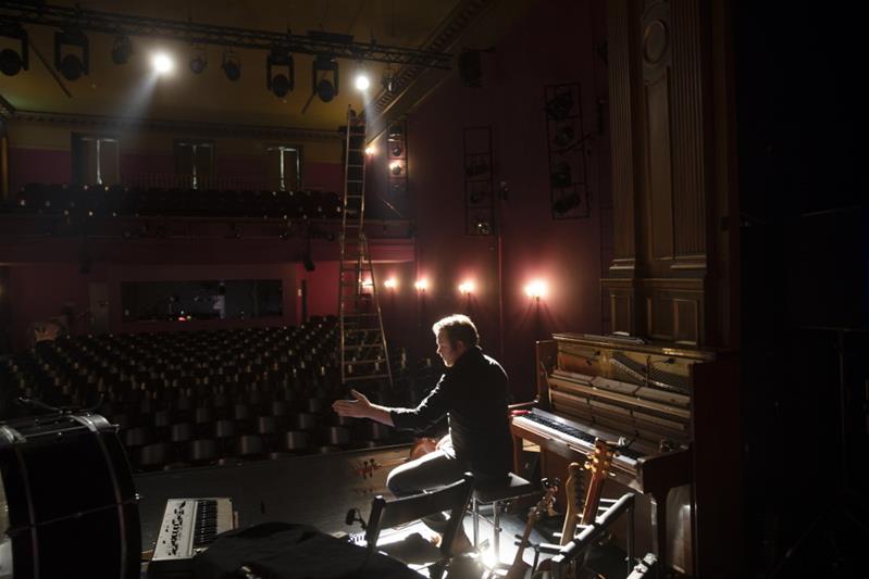 Un homme sur une scène est entouré de plusieurs instruments de musique.