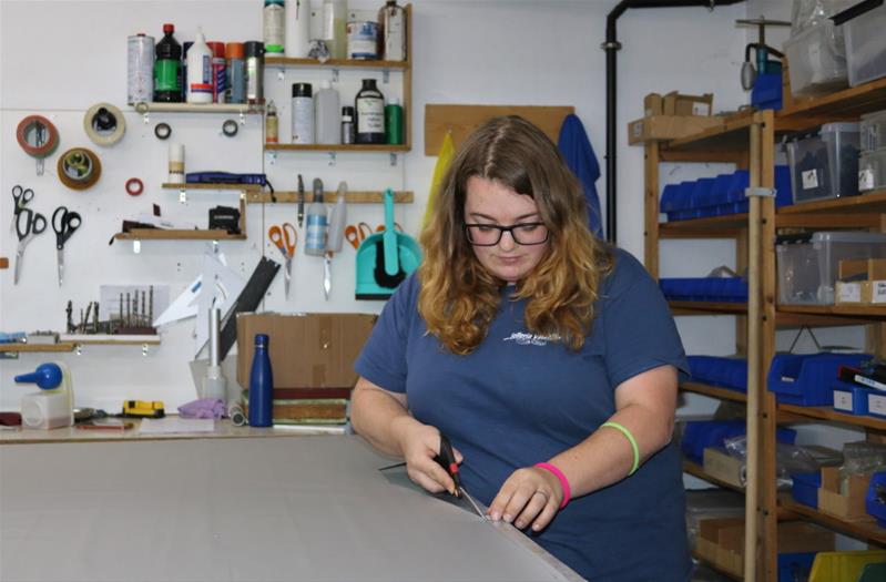 Une femme découpe du cuir sur une table.