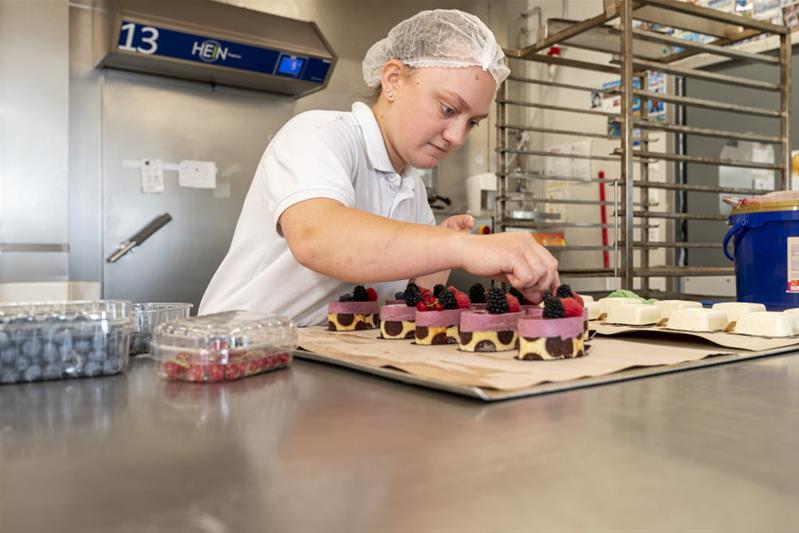 Une apprentie décore des pâtisseries.