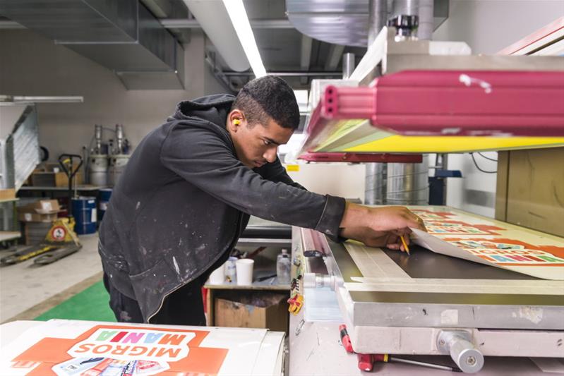 Un apprenti place une feuille dans la machine pour une impression en série.
