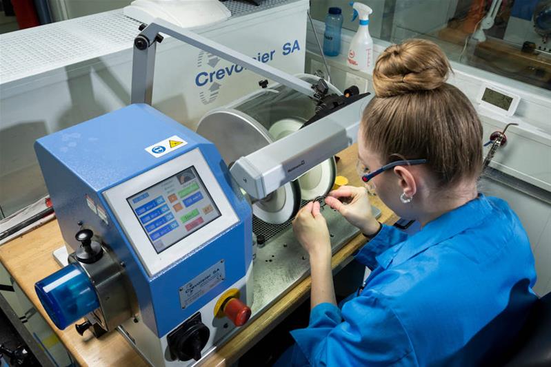 Une apprentie polit une pièce de métal à l'aide d'une machine.