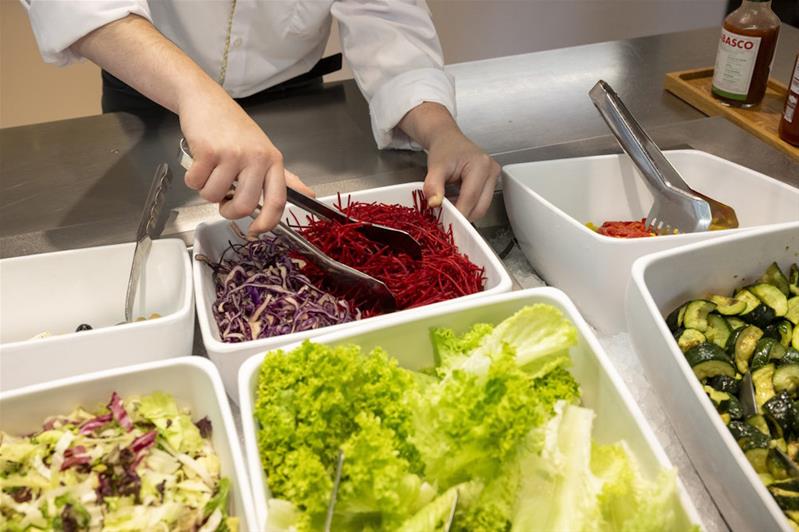 Un apprenti prépare un buffet de salades.