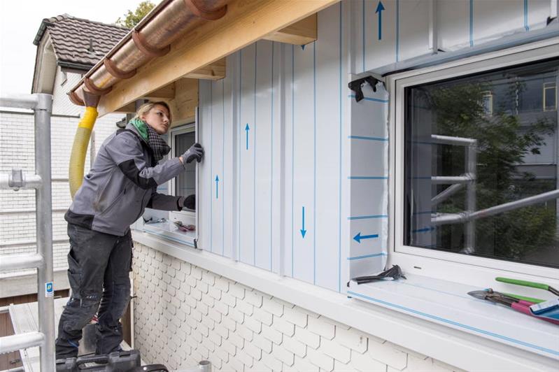 Une ferblantière travaille sur le revêtement d’un mur extérieur.