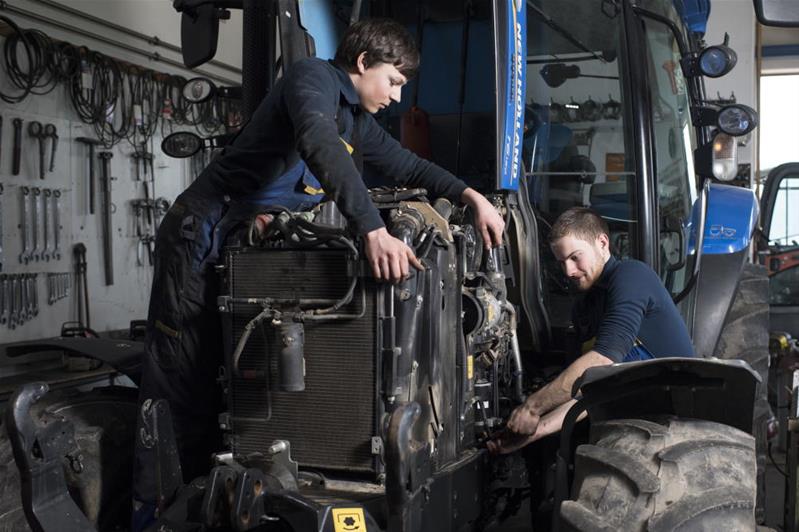 Deux jeunes techniciens réparent le moteur d'un tracteur.