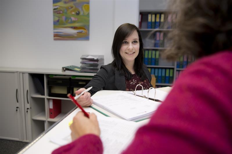 Une spécialiste du secteur des assurances discute avec une deuxième personne avec, devant elle, un classeur ouvert contenant des documents.