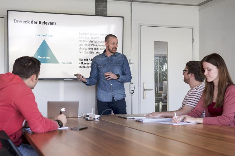 Un homme devant un écran montre un schéma à ses collaborateurs lors d’une séance de travail.