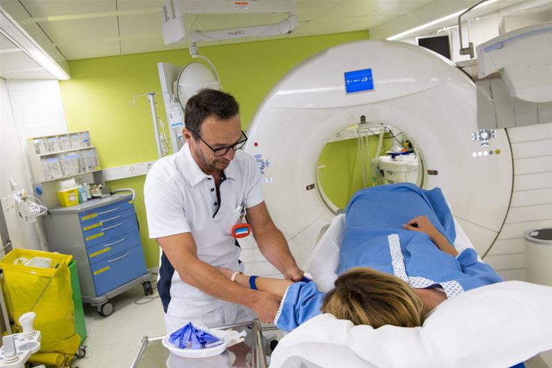 Un homme s’occupe d’une patiente, allongée sur un brancard, avant un examen d'imagerie médicale.
