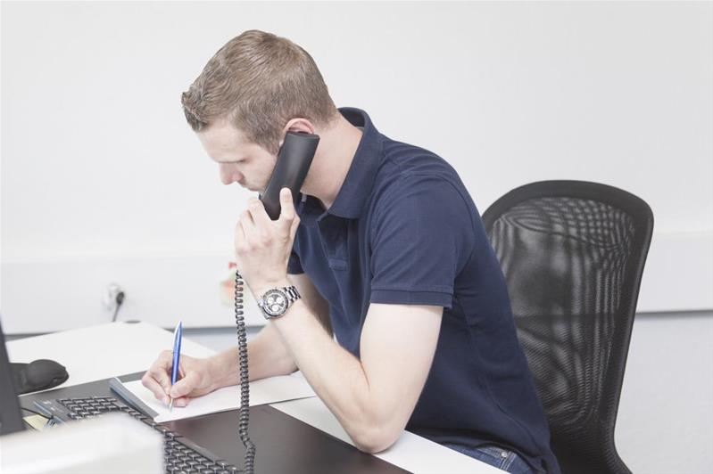 Un jeune homme est au téléphone et prend des notes.