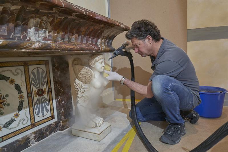 Le conservateur-restaurateur nettoie la surface d'une sculpture à l'aide d'une éponge.