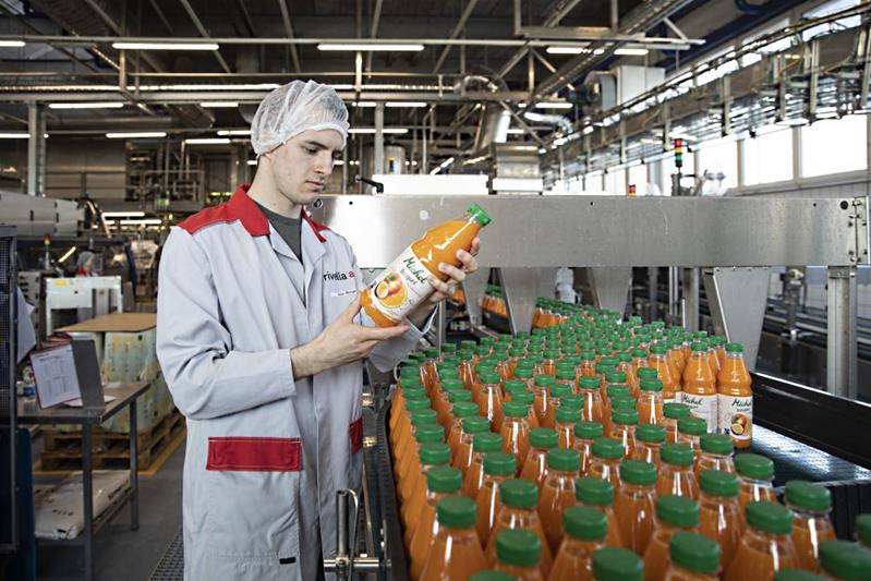Un homme se tient devant une ligne de production de bouteilles de jus de fruits.