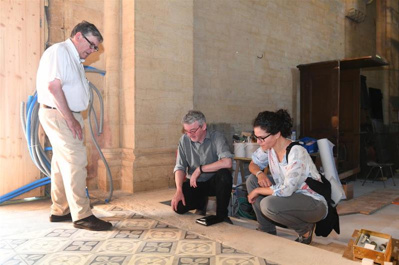 Trois professionnels observent le sol d’un édifice ancien.