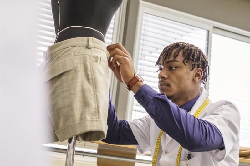 Un jeune couturier prend les mesures d'un vêtement.