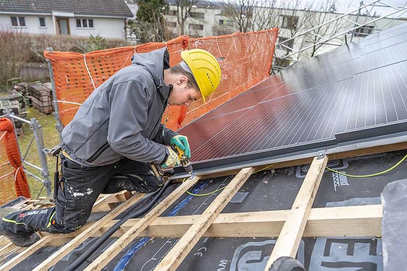 Un apprenti pose des panneaux solaires dur le toit d'une maison.