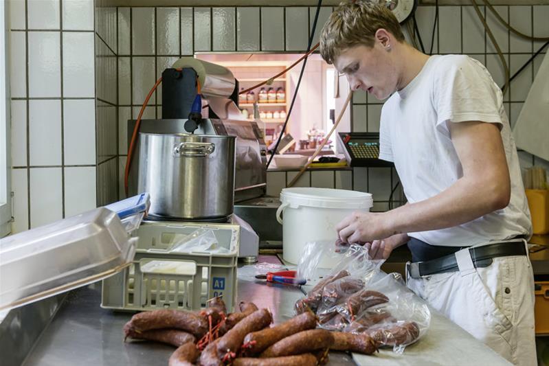 Un apprenti met des saucisses dans un sac en plastique.