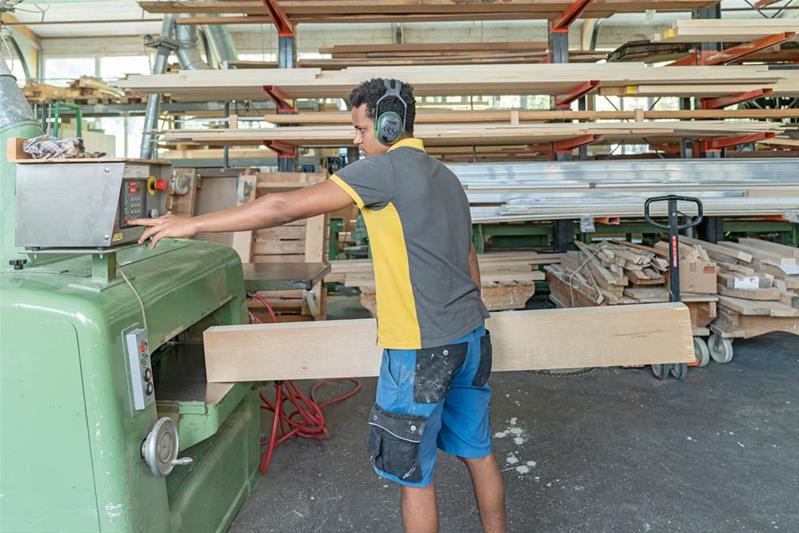 Un apprenti coupe une poutre en bois à l'aide d'une machine.