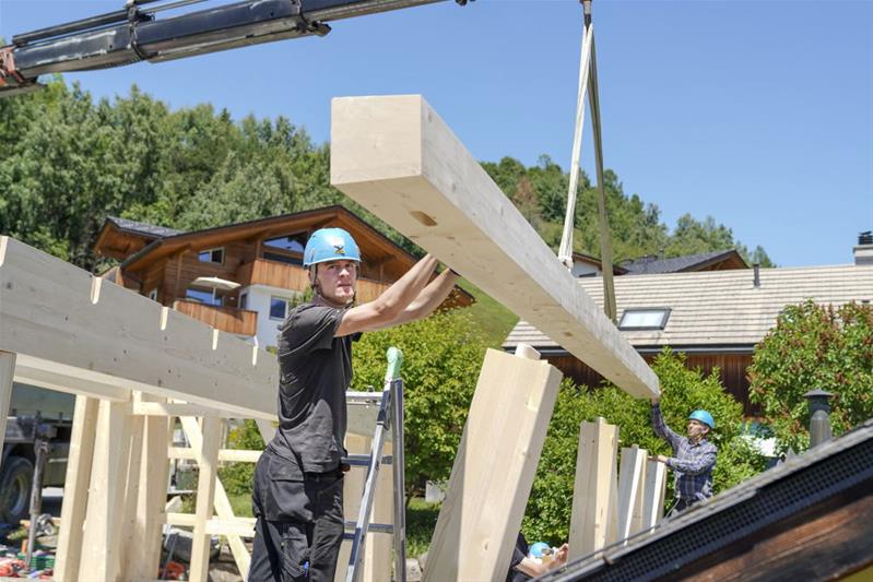 Un apprenti praticien sur bois déplace une poutre sur un chantier à l'aide d'un treuil.