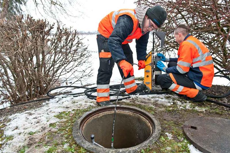 Deux apprentis contrôlent une canalisation au bord d'une route.