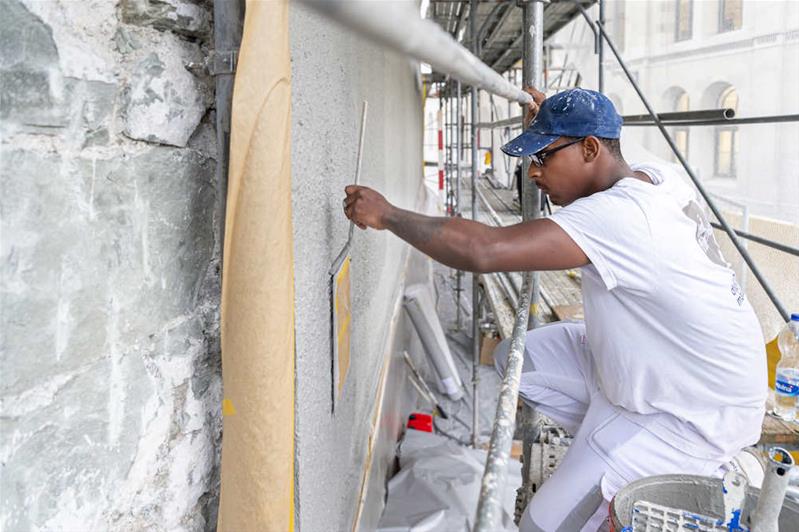 Un apprenti aide-peintre peint une fenêtre.