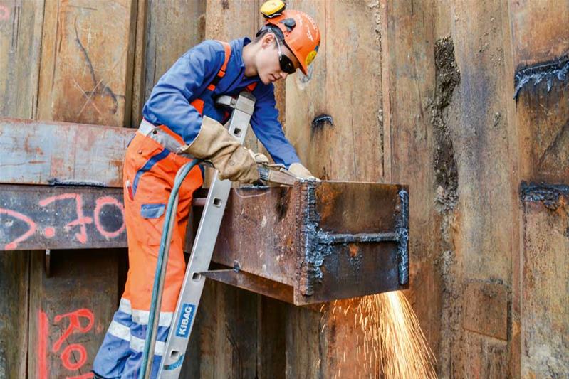 Un apprenti découpe des poutres en métal sur un chantier.