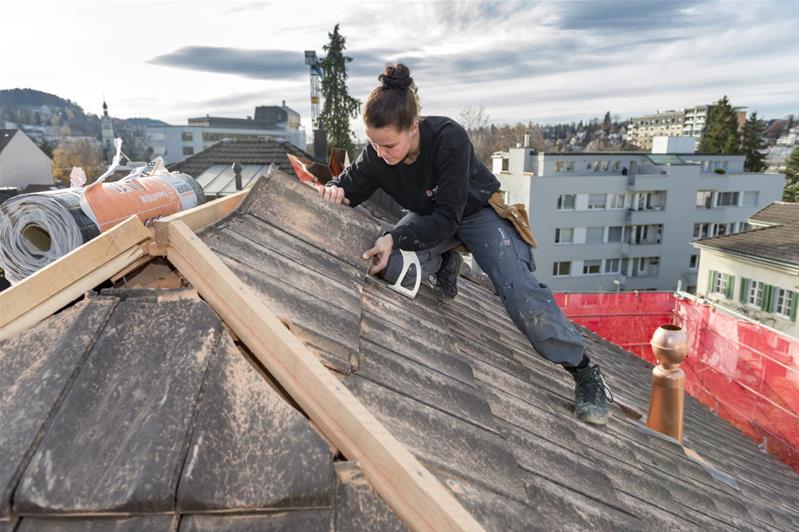Une apprentie pose des tuiles sur un toit.