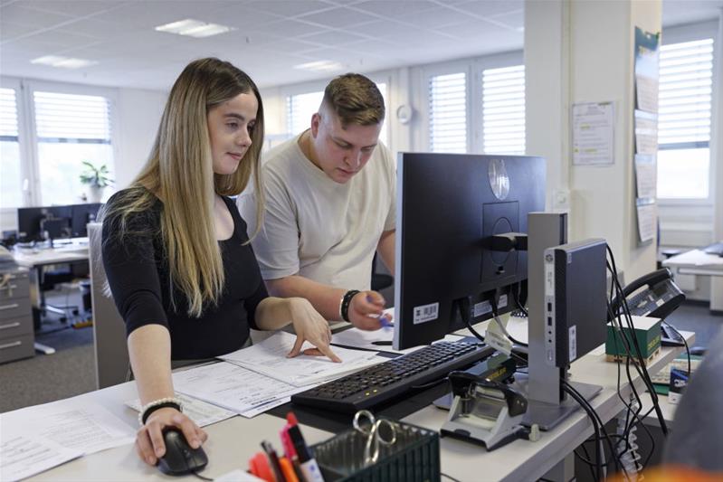 Une apprentie et son collègue travaille au bureau devant un ordinateur.