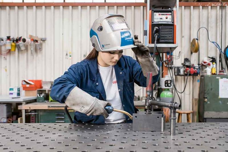 Une apprentie façonne une pièce de métal avec un chalumeau.