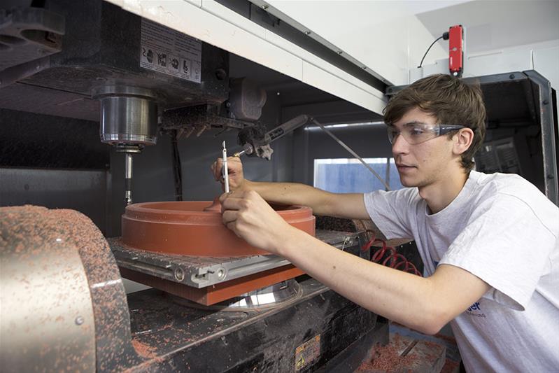 Un apprenti prépare un moule avec une machine.