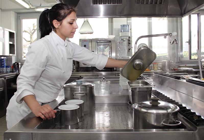 Une apprentie soulève un couvercle pour contrôler la cuisson du plat.