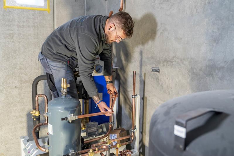 Un apprenti fixe un tuyau sur une installation.