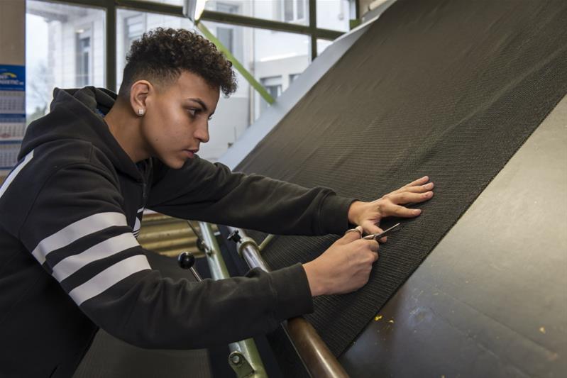 Un apprenti découpe un morceau de tissu avec des ciseaux.