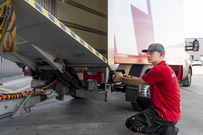 Un apprenti contrôle le camion avant de partir.