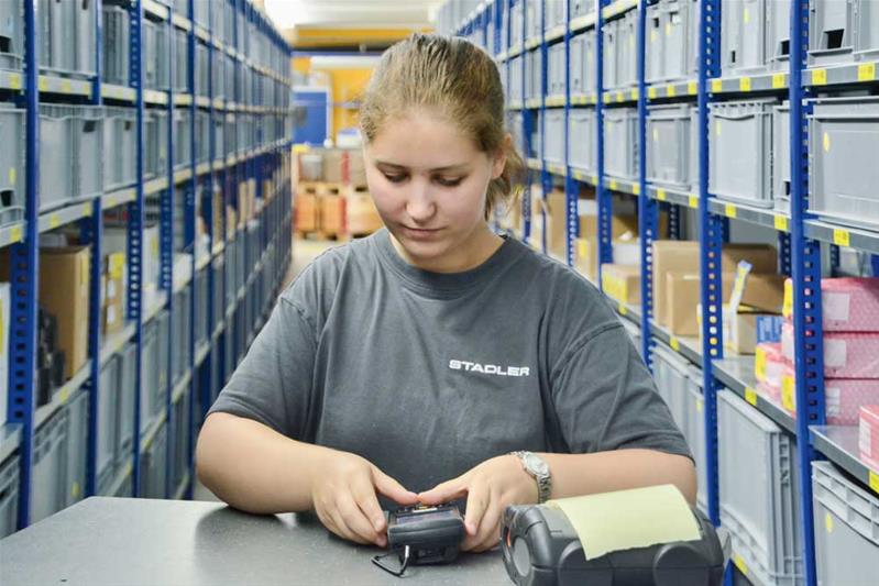 Une apprentie contrôle les produits dans l'entrepôt à l'aide d'un appareil.