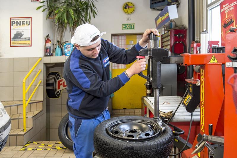 Un apprenti remonte un pneu sur une roue.