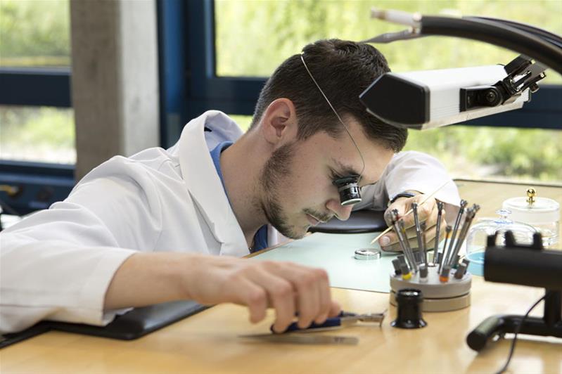 Un homme regarde une pièce d'horlogerie avec une loupe.